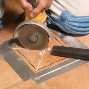 双手紧紧握着磨床,非盟thor carefully plunges the blade into the tile’s center and cuts diagonally, then along the tile’s sides.