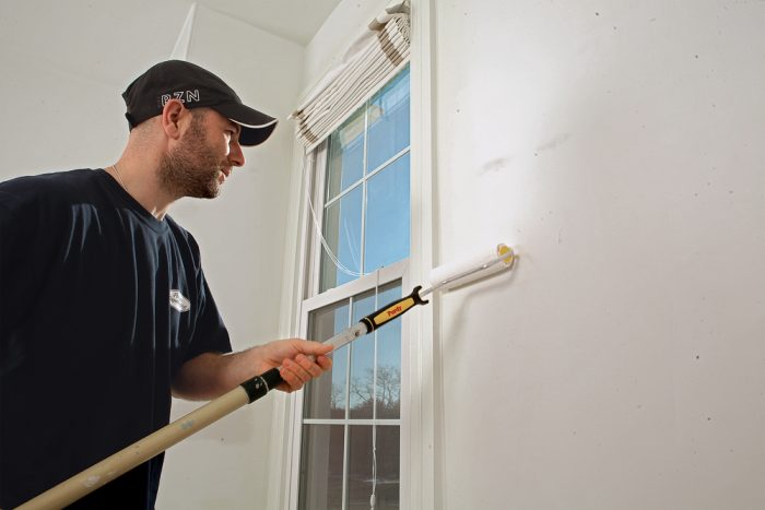 Applying sizing to a surface before wallpapering.